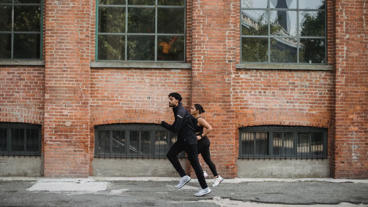 A couple jogging together on a city street beside a red brick wall, showcasing a healthy lifestyle.